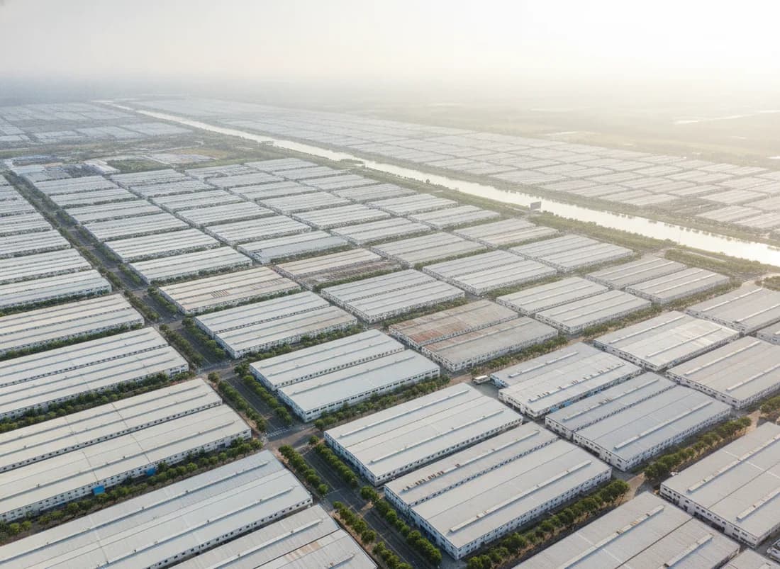 An elevated view over thousands of identical pale workshop roofs in a regular grid running to the horizon, cut by tree-lined avenues and a canal.