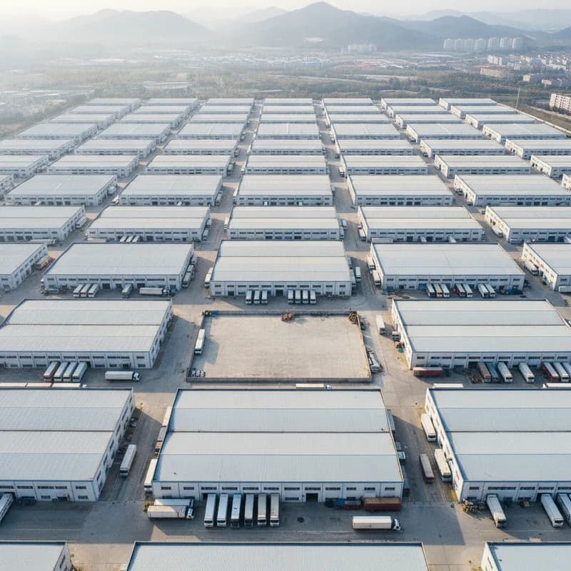 An overhead view of forty near-identical factory sheds on a grid of service roads, one of them standing in an empty yard.